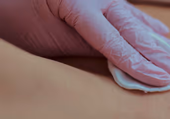 Hand wearing pink medical gloves applying a cotton pad on skin.