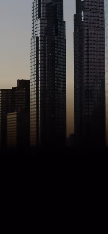 Silhouettes of modern glass skyscrapers against a dim twilight sky.