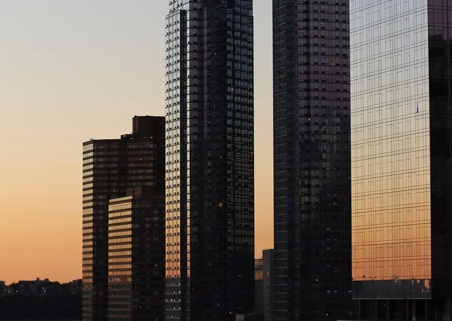 Tall modern buildings reflecting the orange hues of a sunset sky in an urban cityscape.
