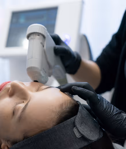 Person receiving a facial treatment with a handheld skincare device by a professional wearing black gloves in a clinical setting.