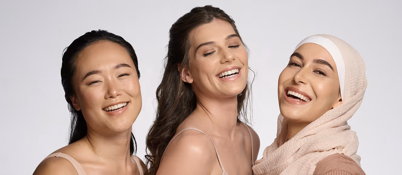 Three diverse women smiling and posing together against a plain background.