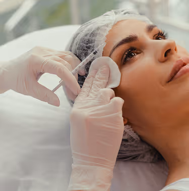 Close-up of a woman receiving a cosmetic injection near her temple by a gloved professional.