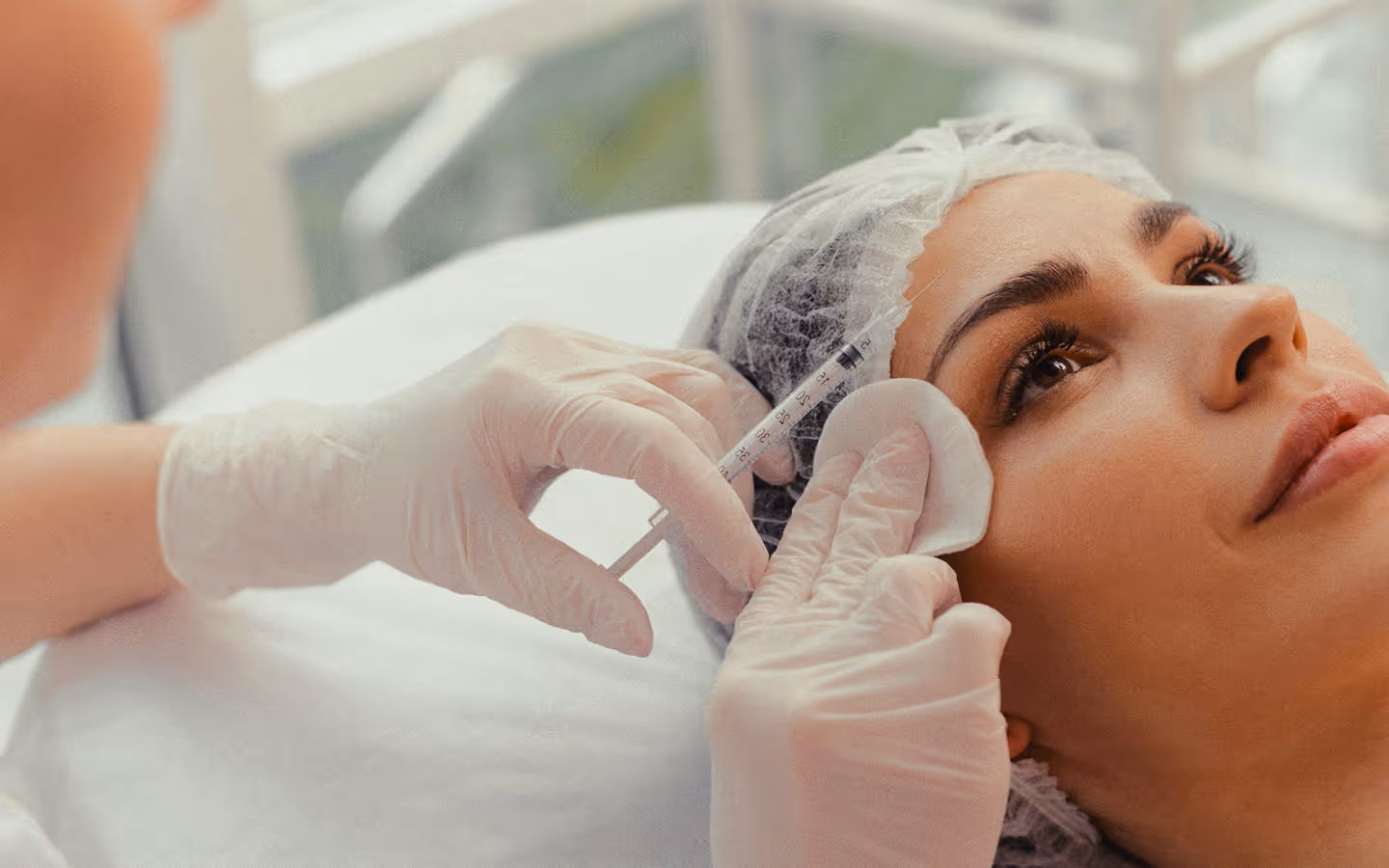 Woman receiving a cosmetic injection on her cheek from a gloved professional in a clinical setting.