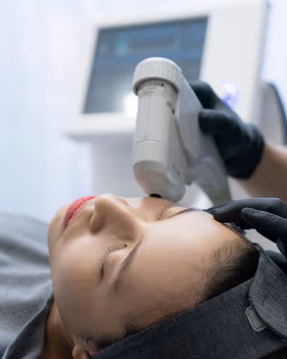 Close-up of a woman receiving a facial treatment with a handheld skincare device by a person wearing black gloves.