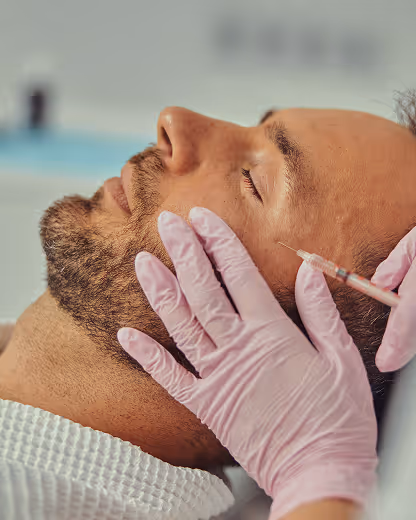 Close-up of a man receiving a facial injection from a person wearing pink gloves.