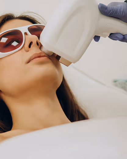 Woman wearing protective eyewear receiving a laser skin treatment on her face from a gloved technician.