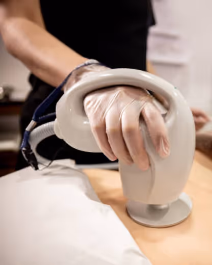 Gloved hand holding a handheld device performing a skin treatment on a person's abdomen.
