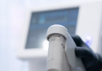 A gloved hand holding a pipette in front of a blurred laboratory device screen.