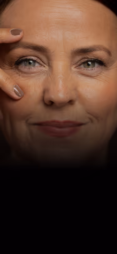 Close-up of a smiling middle-aged woman with green eyes touching her face gently with manicured fingers.