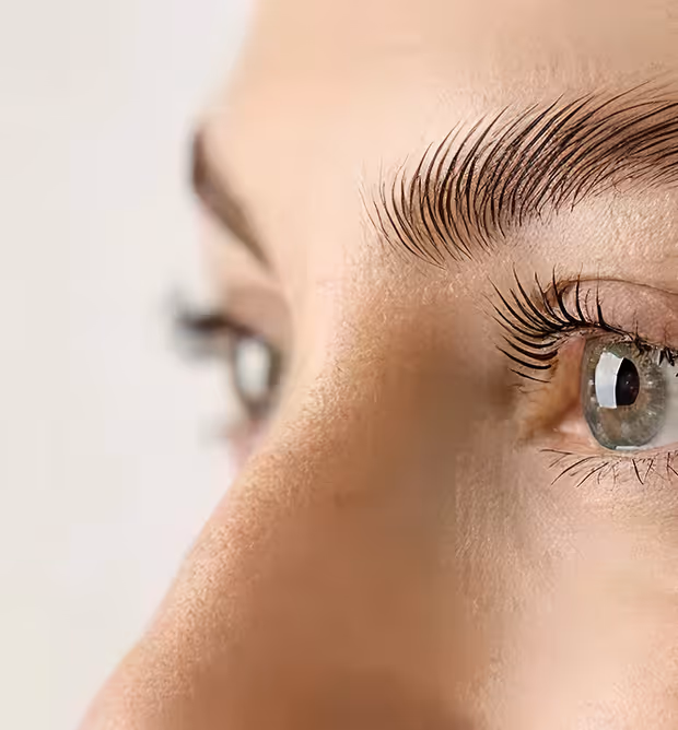 Close-up side view of a person's green eye with long eyelashes and well-defined eyebrow on fair skin.