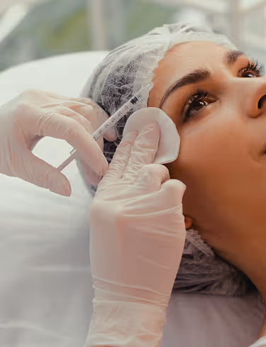 Close-up of a woman receiving a cosmetic injection near her temple by a gloved professional.