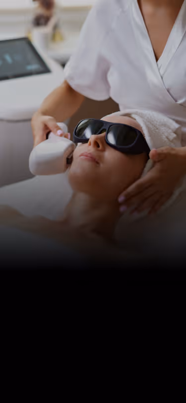 Woman wearing protective goggles receiving facial laser treatment from a technician.