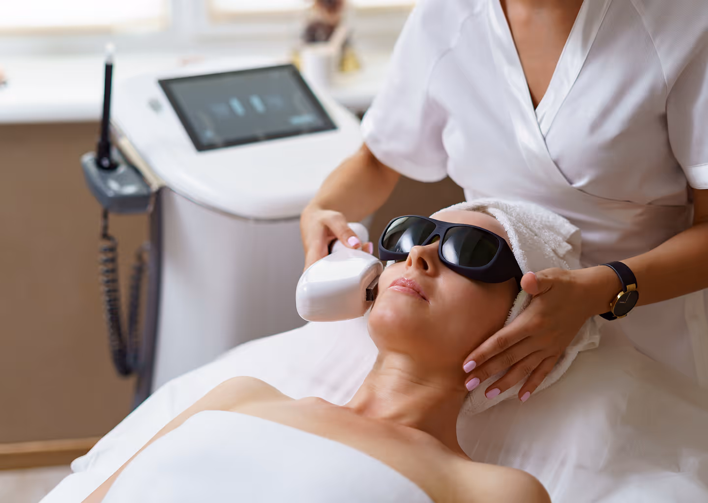 Woman wearing protective glasses receiving facial laser treatment from a technician in a spa.