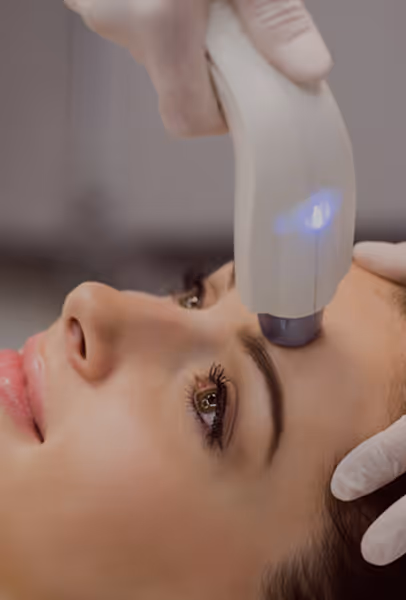 Close-up of a woman receiving a facial treatment with a handheld device near her forehead.