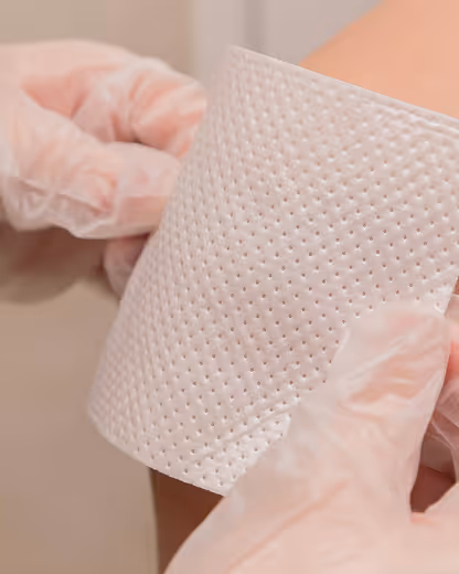 Hands wearing gloves applying a textured adhesive patch to a person's skin.