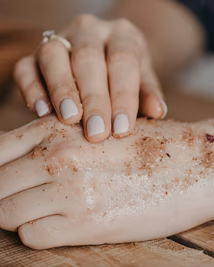 Close-up of a hand applying a scrub with coarse grains on the back of another hand.