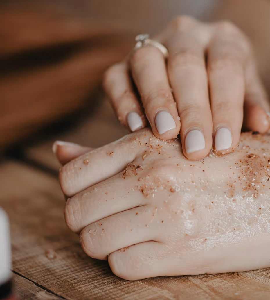 Close-up of hands with exfoliating scrub on skin over wooden surface.