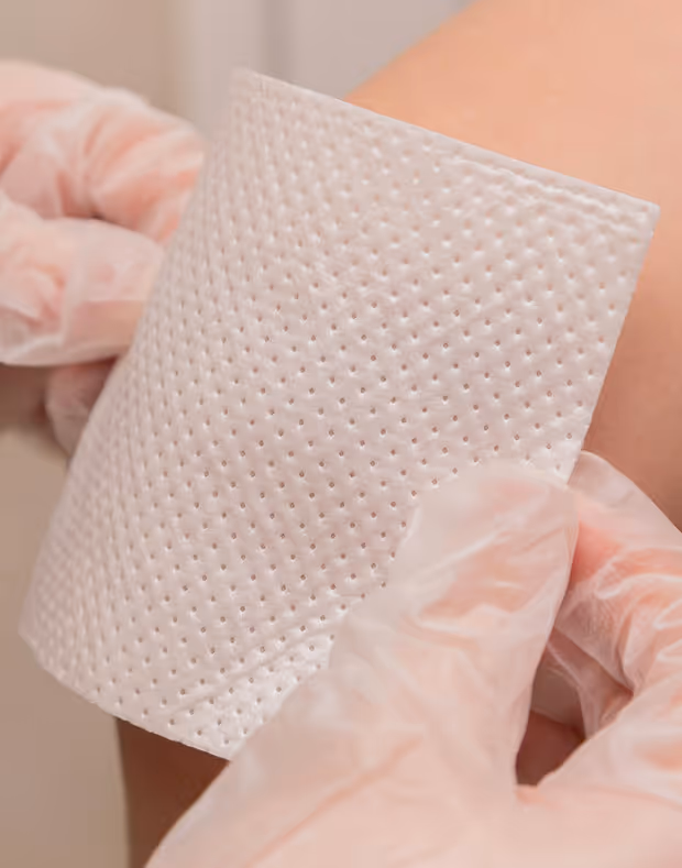 Gloved hands applying a textured adhesive patch to skin.