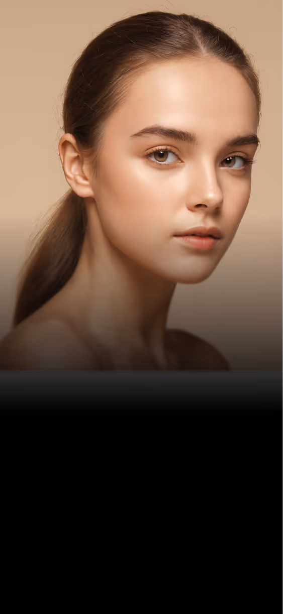 Close-up portrait of a young woman with smooth skin and tied-back hair against a beige background.