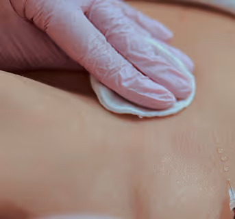 Gloved hand pressing cotton pad on skin near a syringe needle for injection.