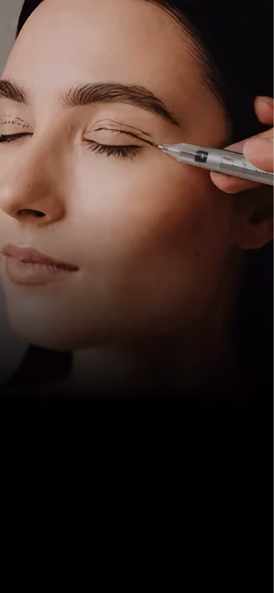 Close-up of a woman having eyeliner tattoo applied on her closed eyelid with a handheld device.