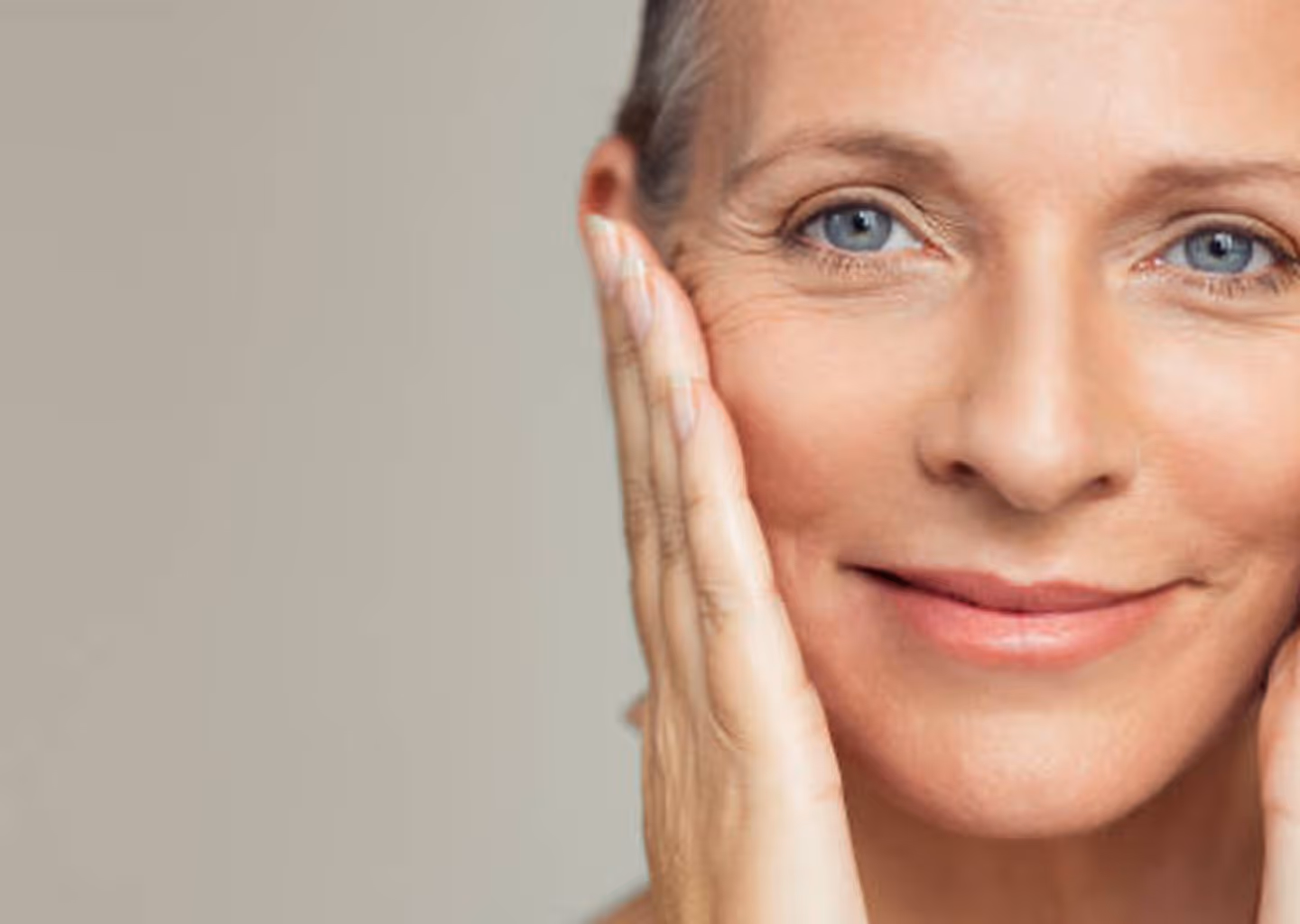 Close-up of a middle-aged woman with clear skin gently touching her face and smiling.