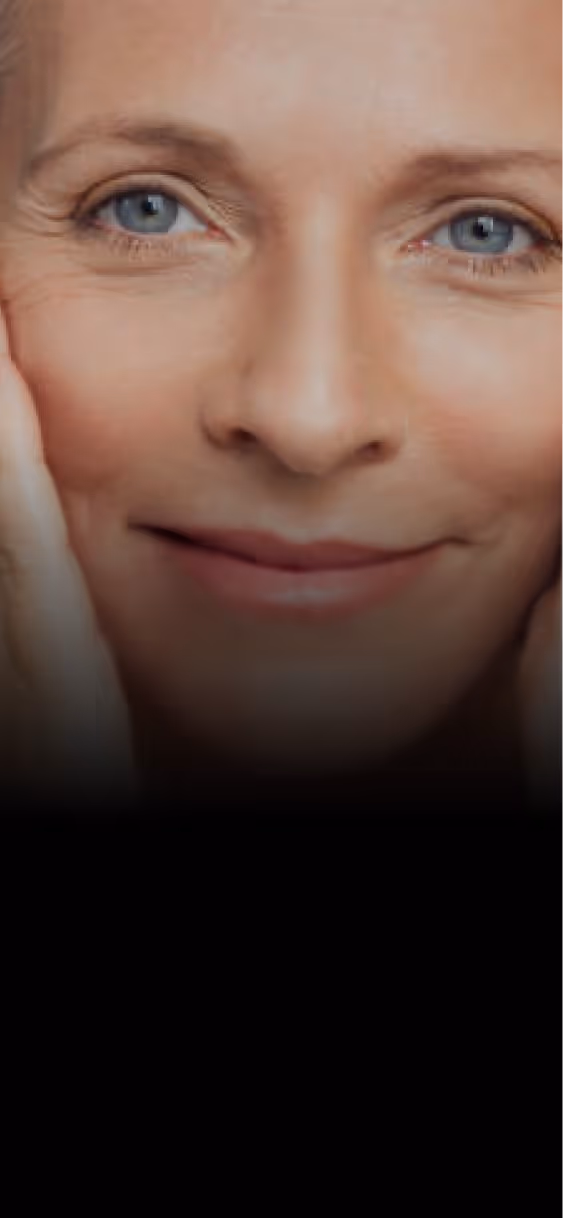 Close-up of a smiling woman with blue eyes gently holding her face.