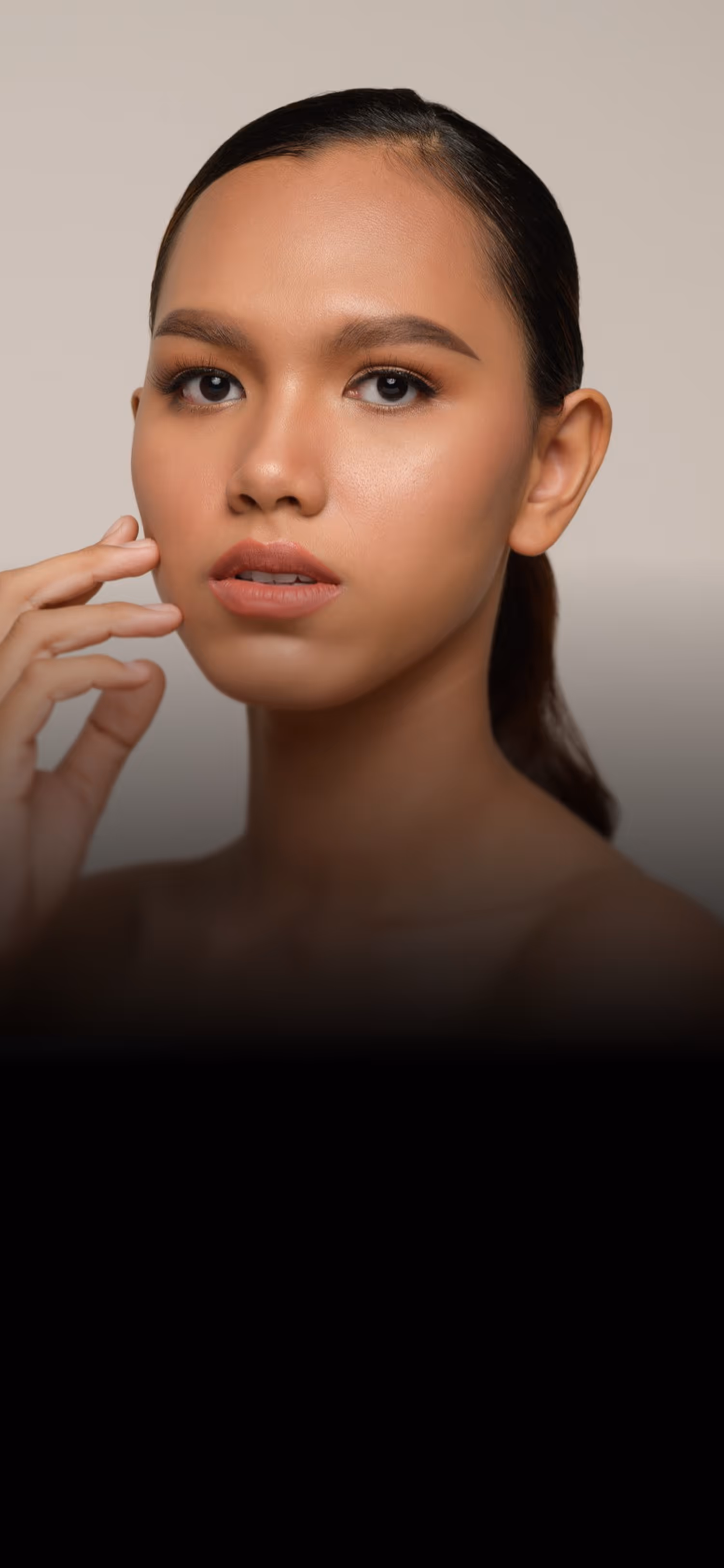 Close-up of a woman with smooth skin, light makeup, and her hand near her face.