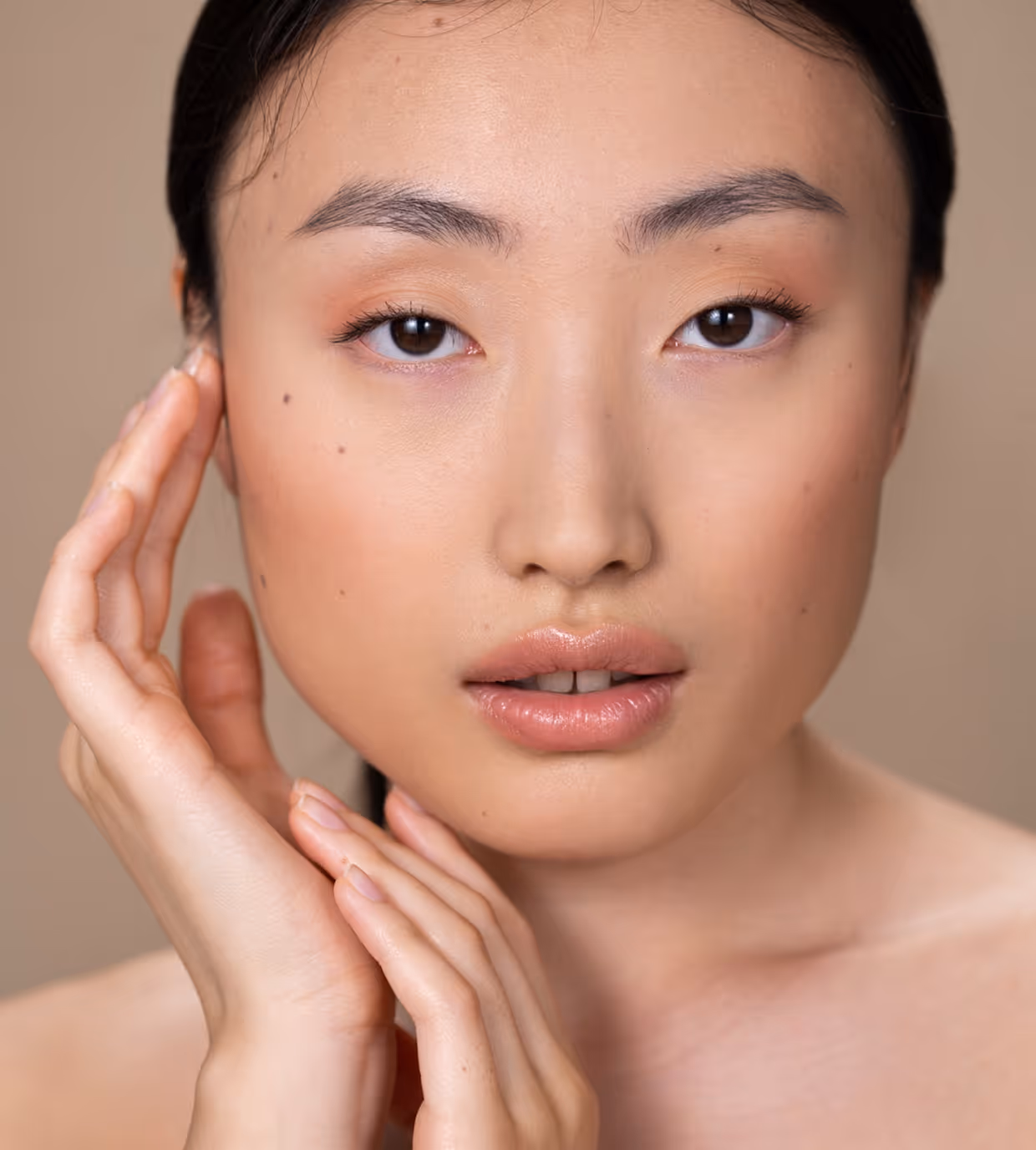 Close-up of a woman with clear skin gently touching her face with both hands.