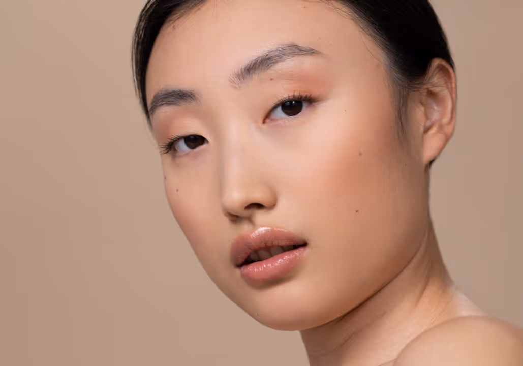 Close-up of a woman's face with natural makeup and smooth skin against a beige background.