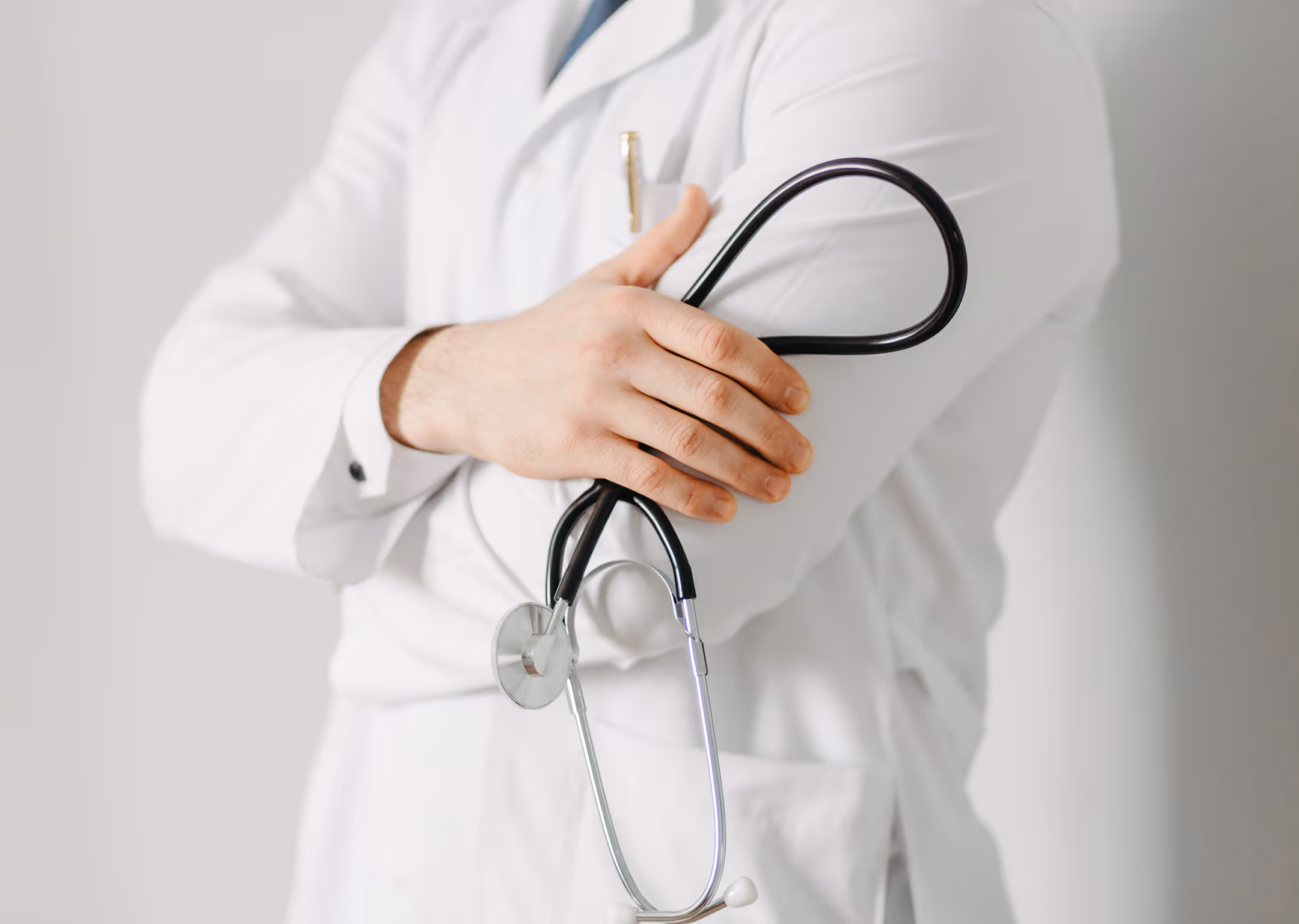 Doctor in a white coat holding a black stethoscope wrapped around their arm.