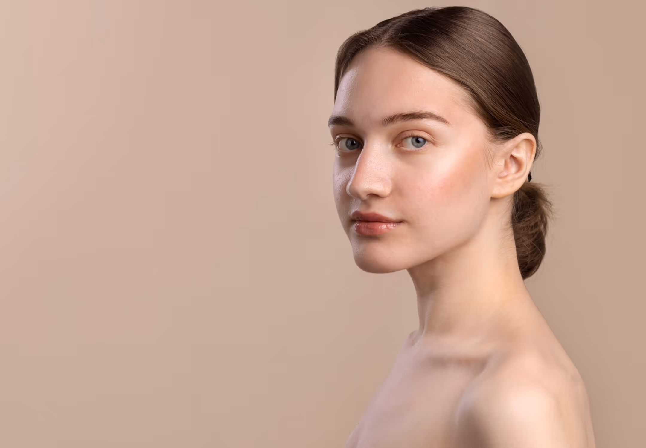 Young woman with light skin, blue eyes, and brown hair tied back against a beige background.