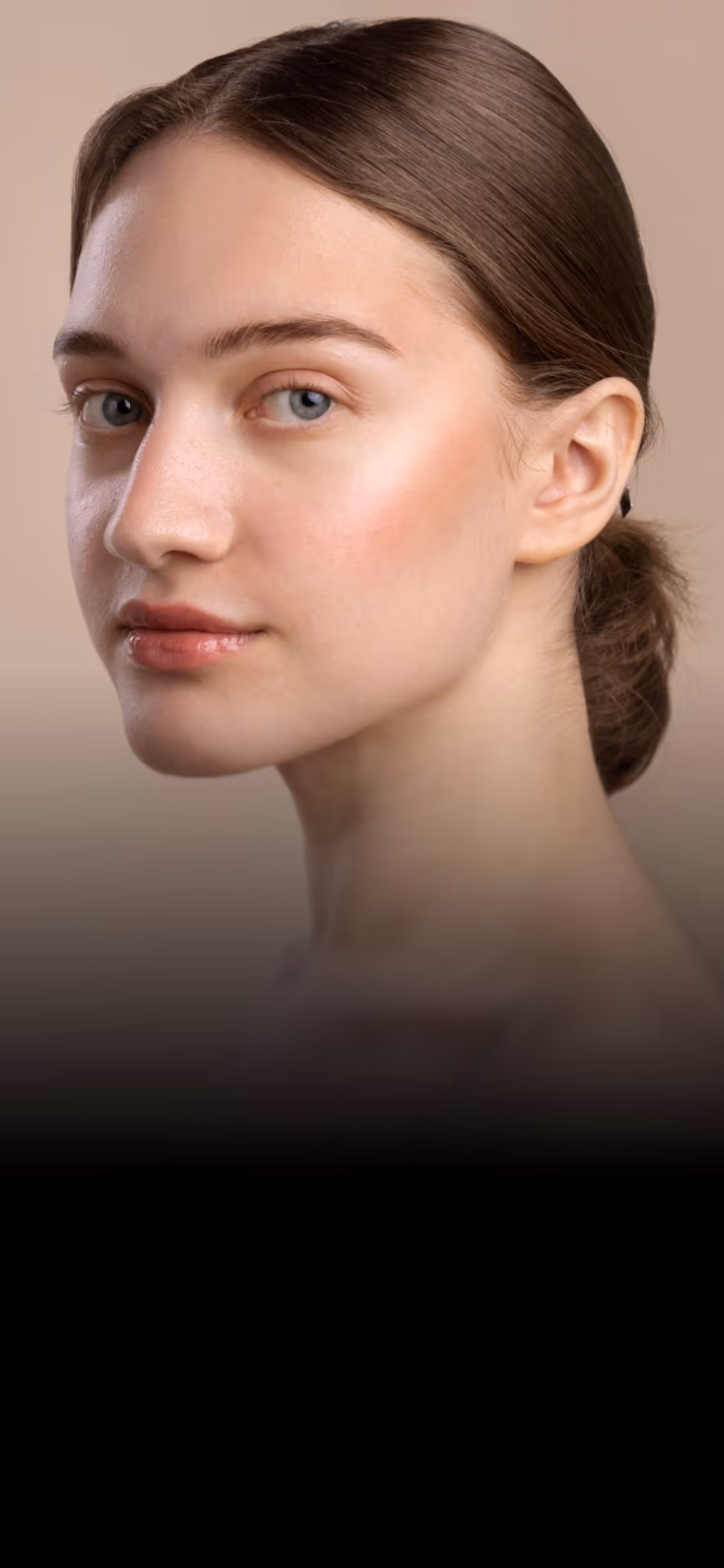 Close-up of a young woman with smooth skin and hair tied back against a beige background.
