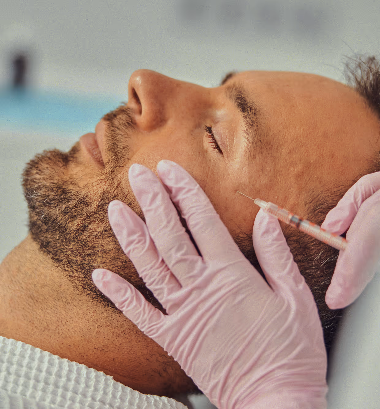 Man with closed eyes receiving facial injection from gloved hands in a clinical setting.