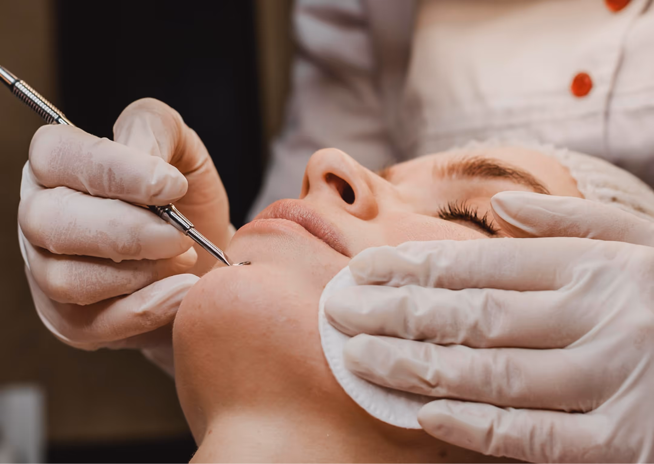 Person receiving professional skin care treatment with gloves and a metal skincare tool on the chin.