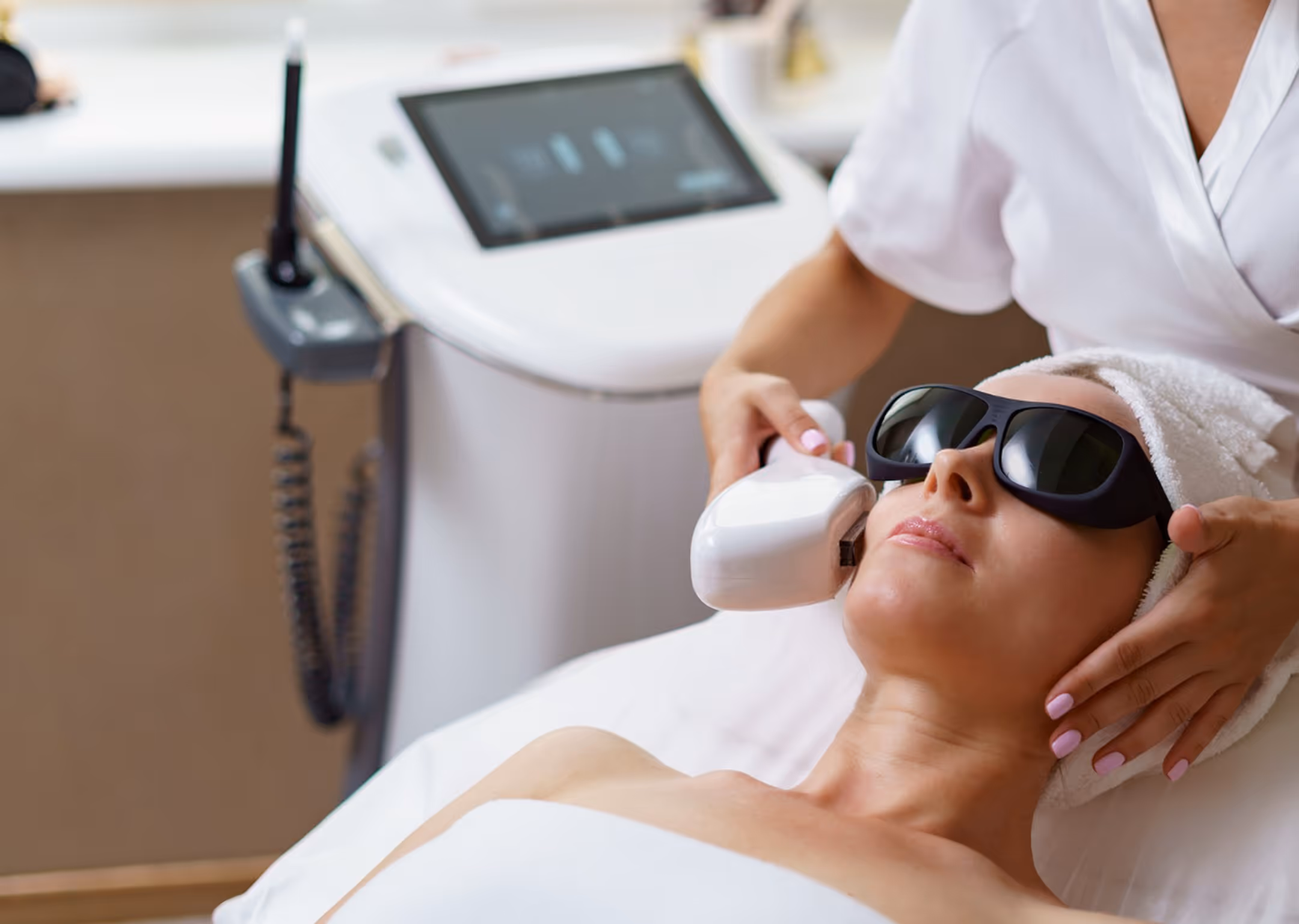 Woman wearing sunglasses getting a laser skin treatment on her face at a spa clinic.