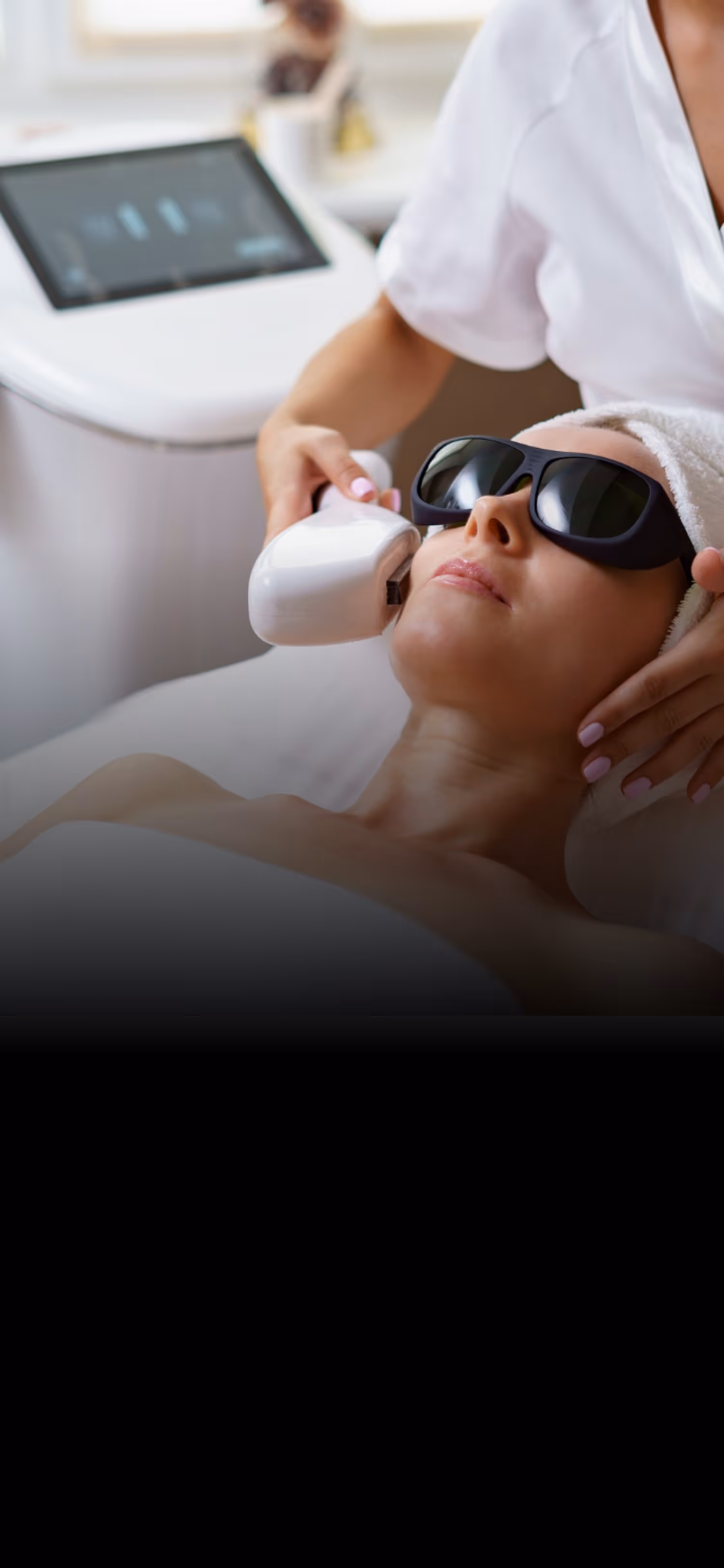 Woman wearing sunglasses receives laser skin treatment on her face from a professional in a clinic.