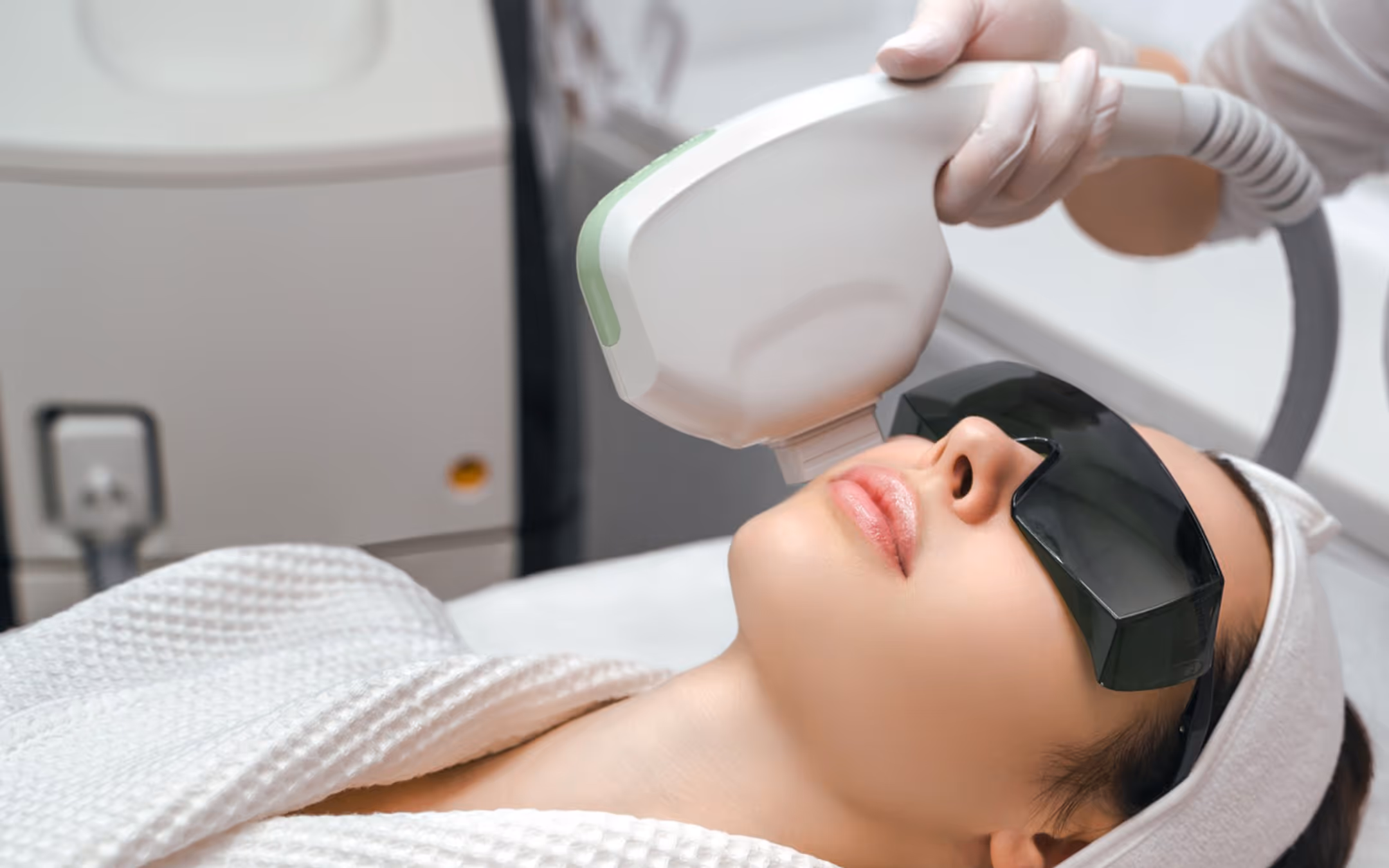 Woman wearing protective glasses getting a laser or light therapy facial treatment in a clinic.