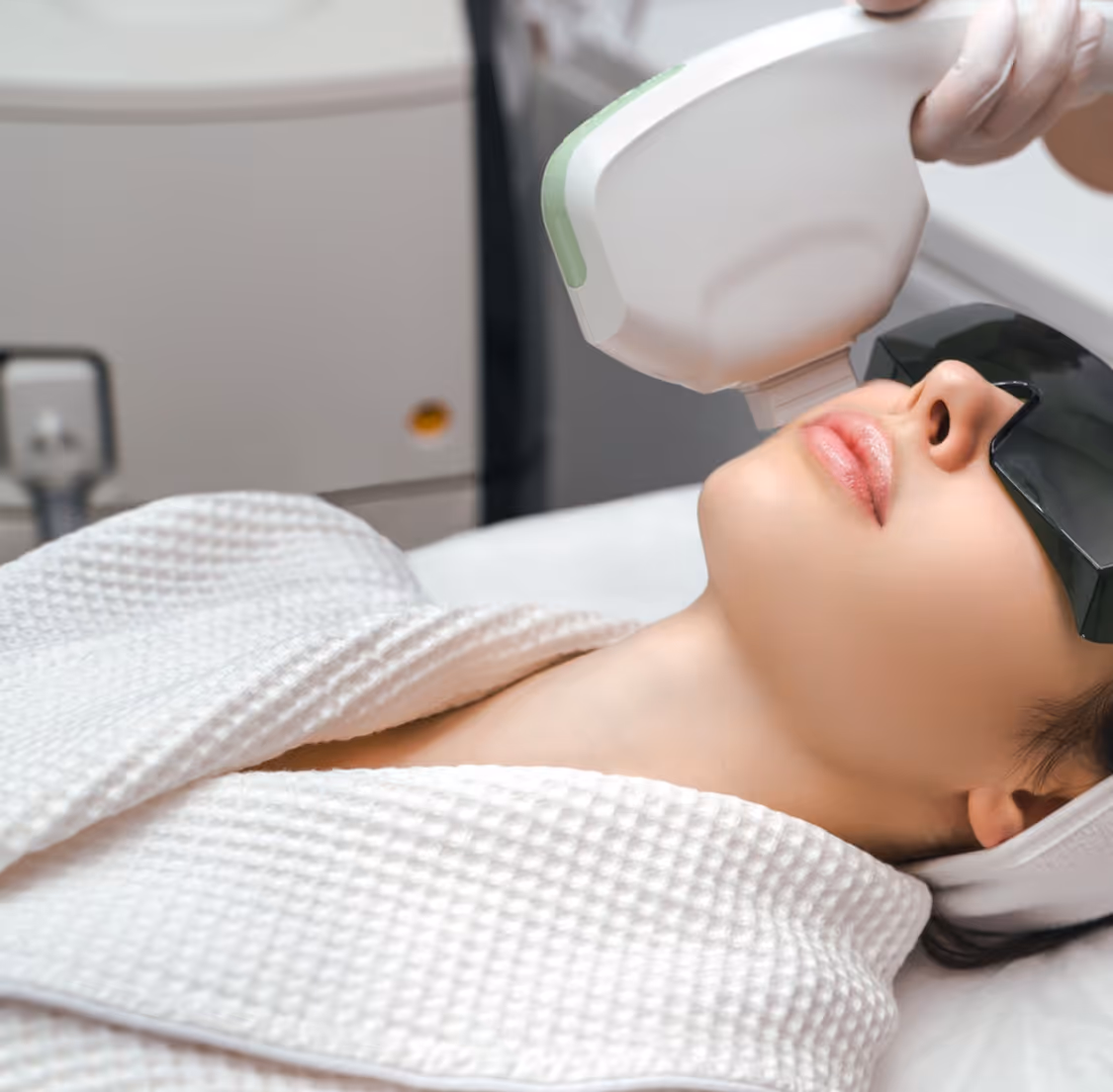 Woman wearing protective glasses receiving a laser skin treatment on her face at a clinic.