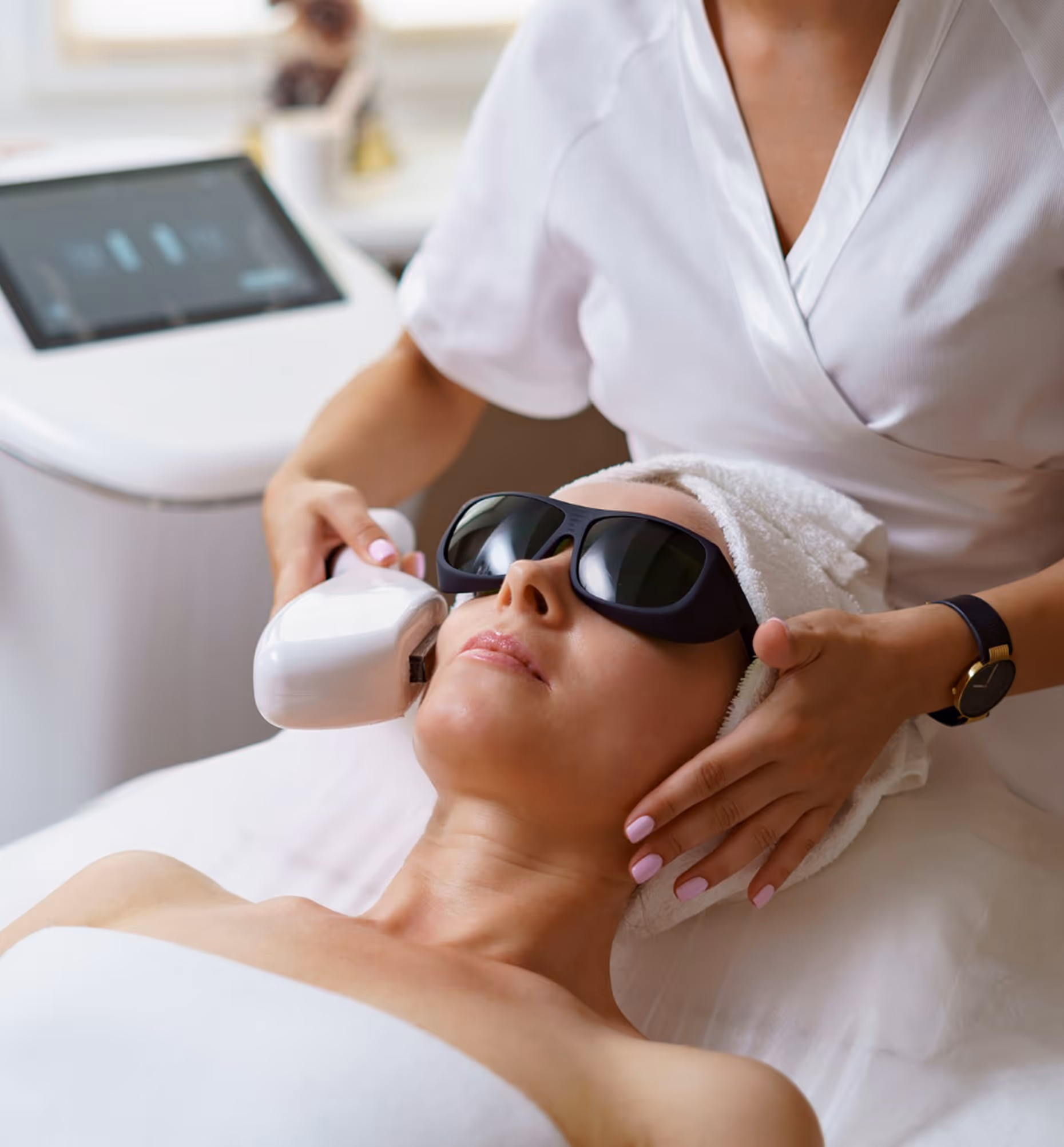 Woman wearing protective goggles receiving facial laser treatment from a cosmetologist in a spa.