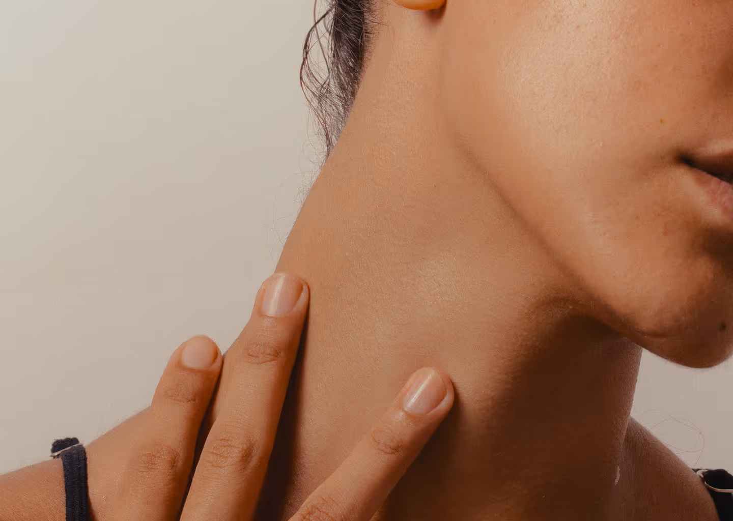 Close-up of a person’s fingers gently touching the side of their neck and jawline.