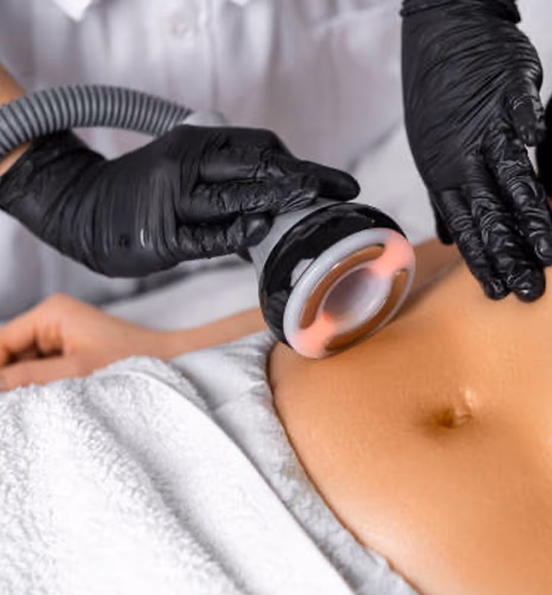 Person receiving a non-invasive body treatment on the abdomen with a handheld device by a gloved technician.