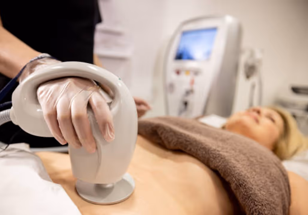 Person receiving non-invasive body contouring treatment on abdomen with a handheld device.