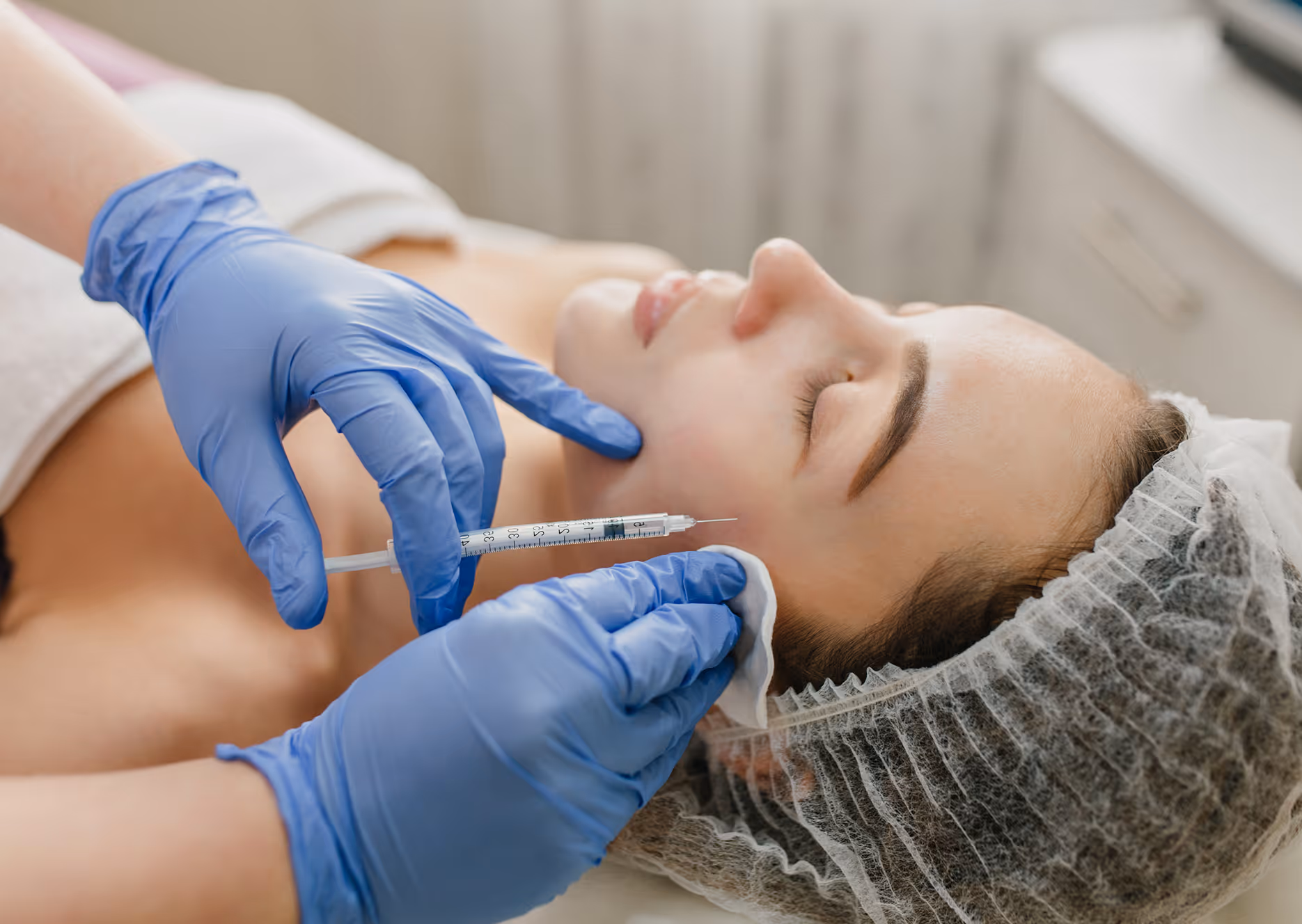 Woman receiving facial injection from a professional wearing blue gloves in a skincare clinic.