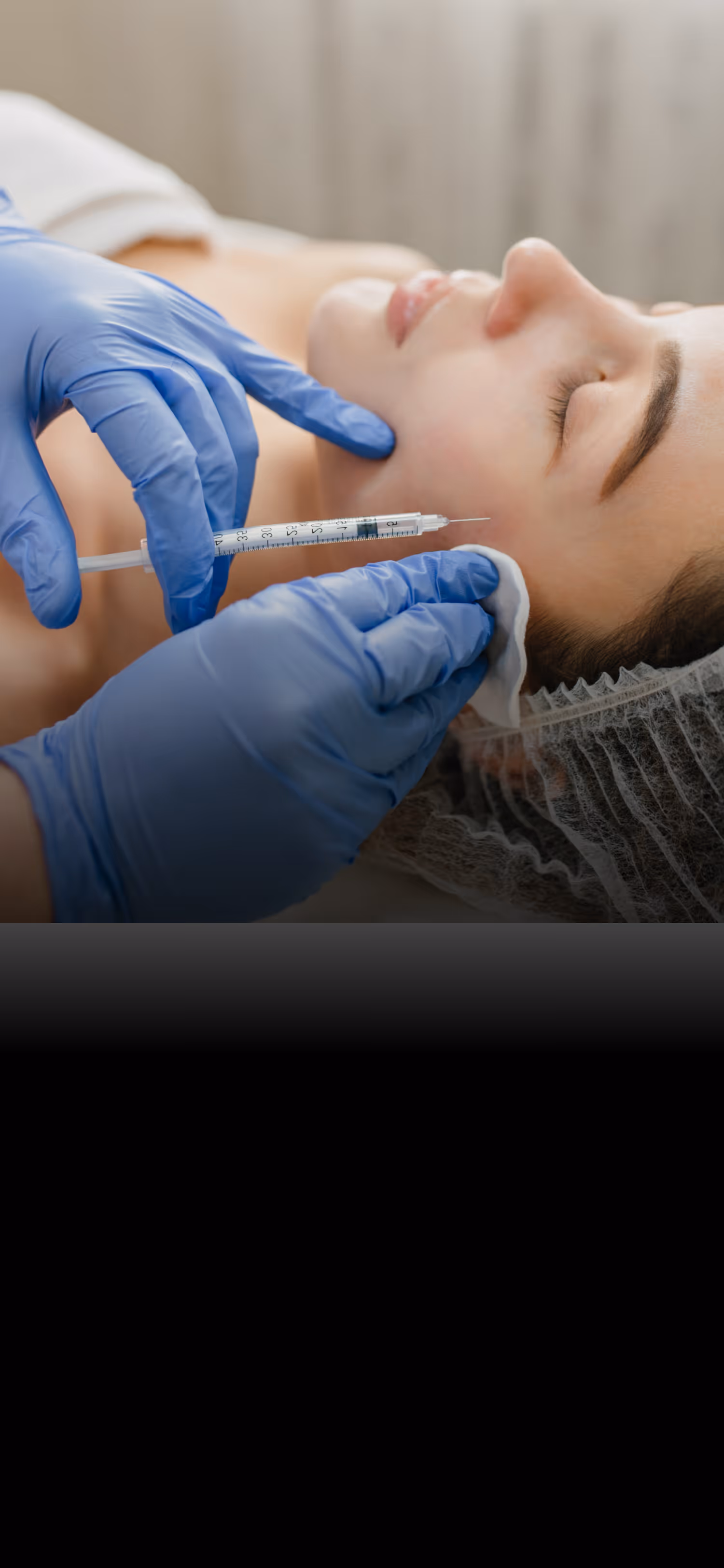 Gloved hands preparing to inject a syringe into a woman's cheek during a cosmetic treatment.