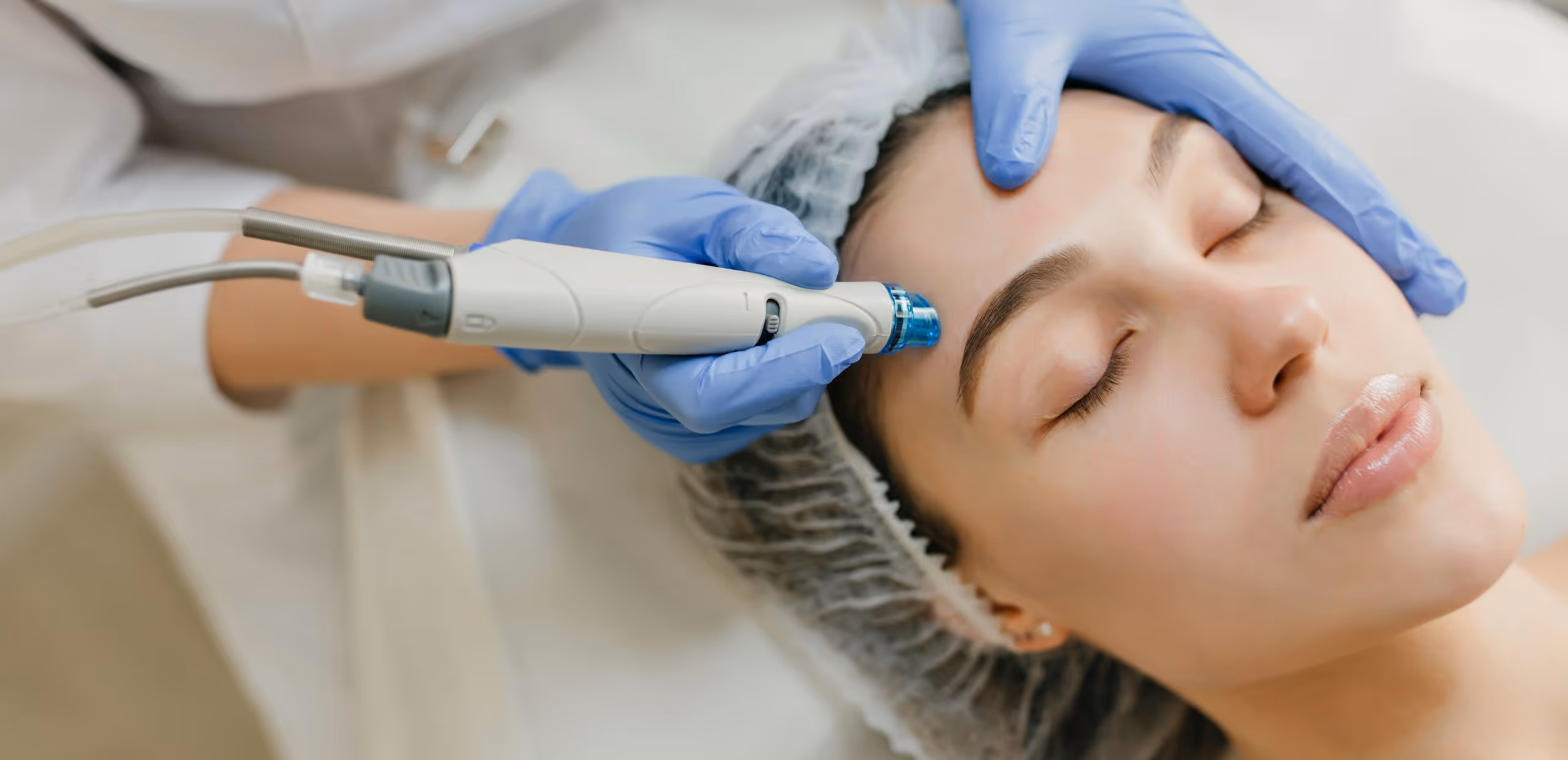 Woman receiving facial microdermabrasion treatment with a handheld device by a gloved specialist.