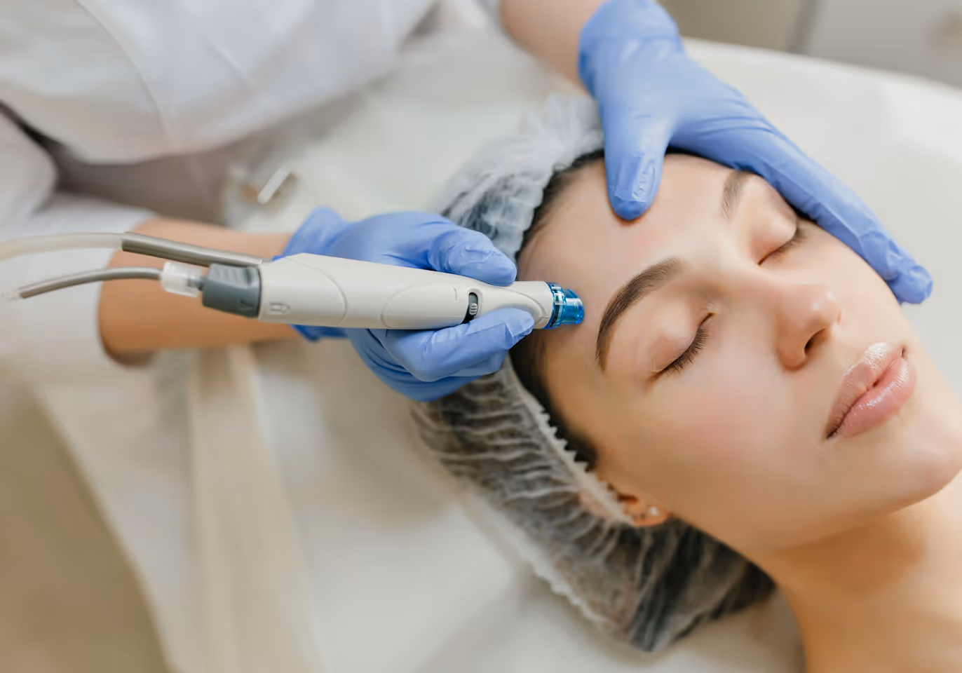 Woman receiving a facial treatment with a handheld device by a technician wearing blue gloves.