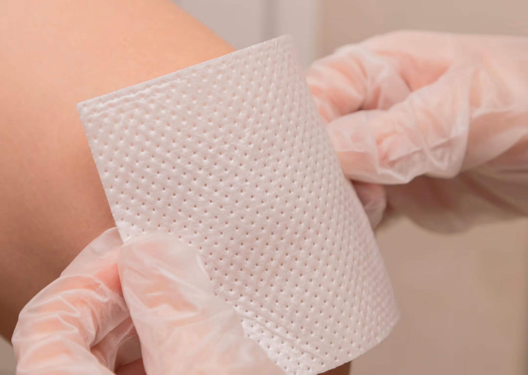 Gloved hands applying a white textured adhesive patch to a person's skin.
