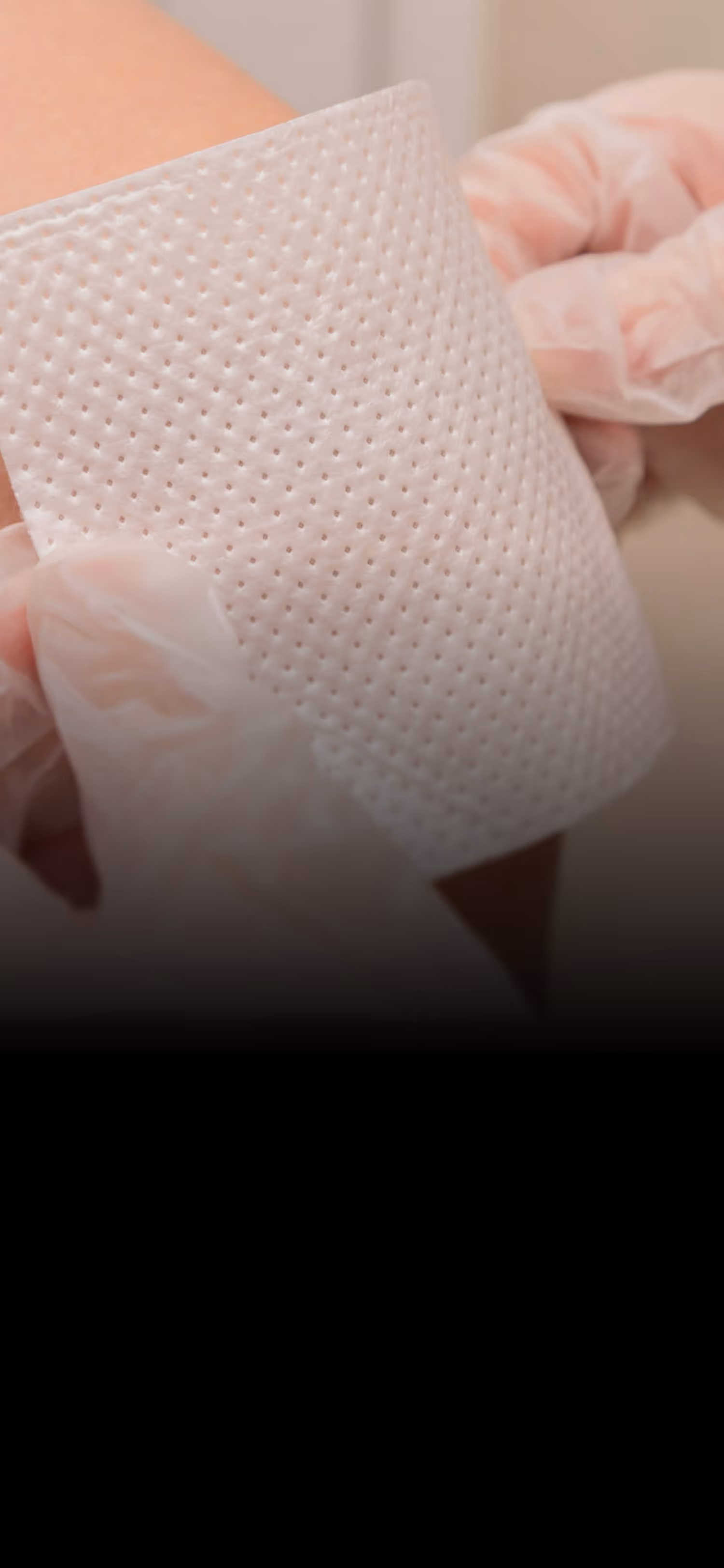Gloved hands applying a perforated adhesive bandage to a person's skin.
