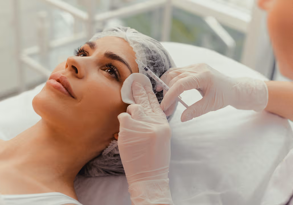 Woman receiving a cosmetic injection near her temple from a gloved professional.